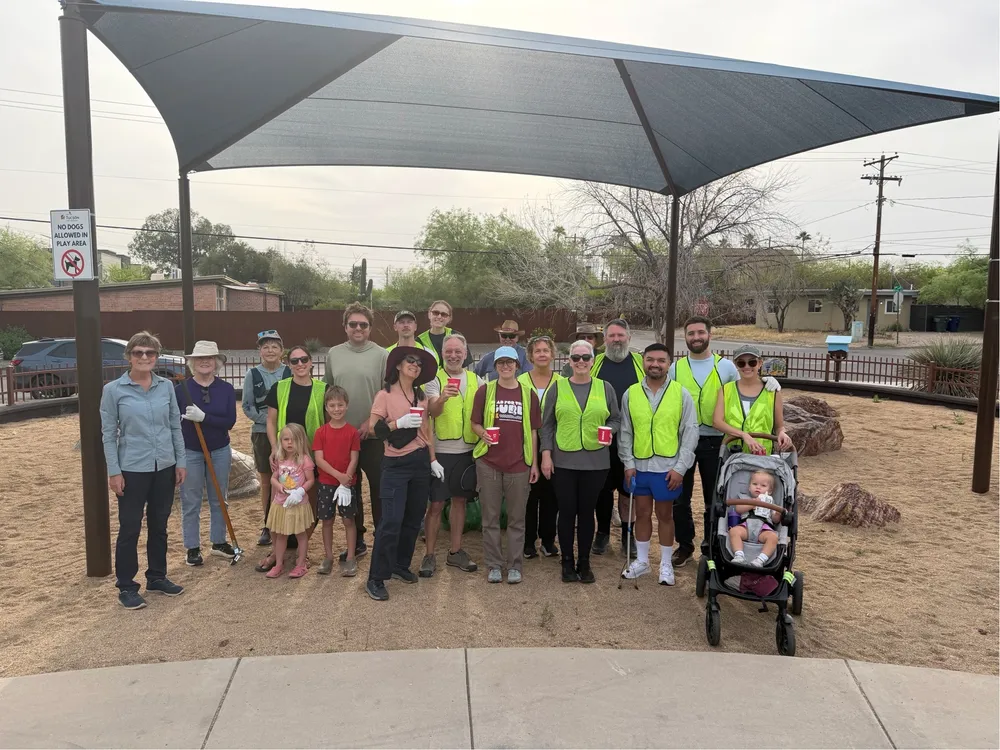 Volunteers in yellow vests gathered under the Pocket Park shade structure after a neighborhood cleanup